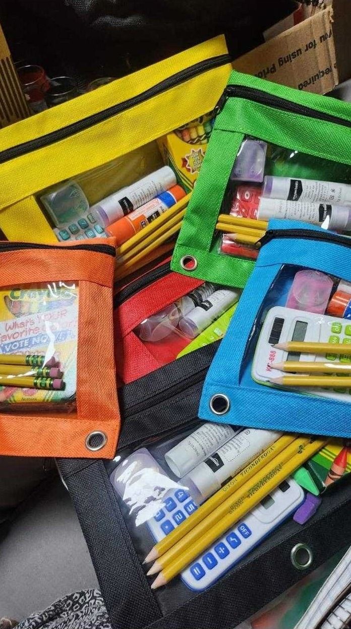 Colorful zippered pouches filled with pencils, glue sticks, crayons and calculators prepared as school supply kits