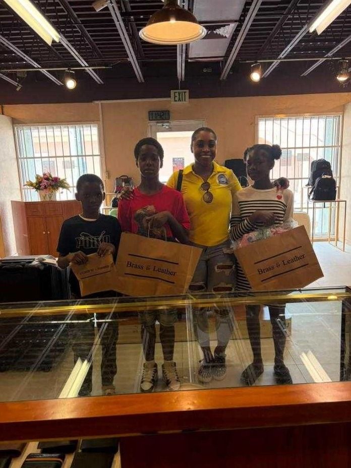 A woman in a yellow polo stands with three children holding Brass and Leather shopping bags inside a store