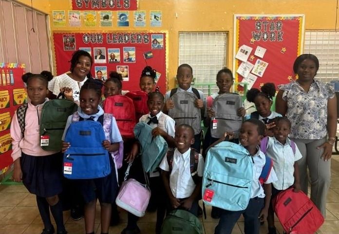 Smiling schoolchildren in uniforms hold new backpacks with two teachers in a decorated classroom