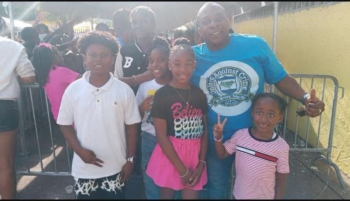 A man in a United Against Crime shirt poses with four smiling children at a barrier