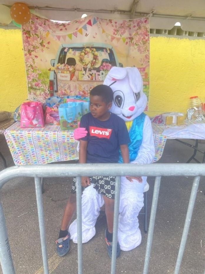A boy sits on the lap of a costumed Easter Bunny in front of an Easter photo backdrop
