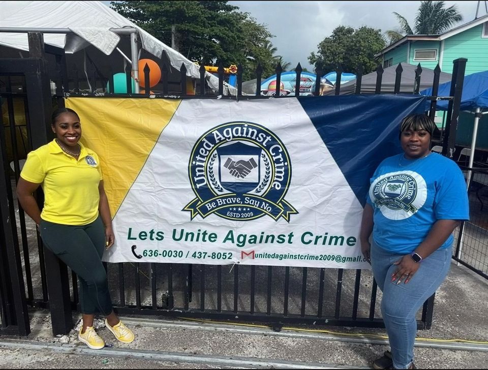 Two women stand beside the United Against Crime banner hung on a black gate at the Easter event