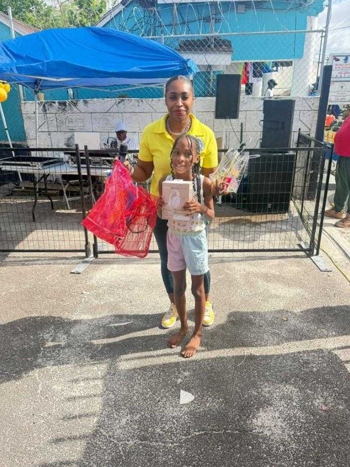 A woman in a yellow polo stands with a smiling girl holding a boxed gift and a red mesh bag