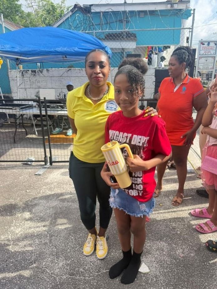 A girl in a red shirt holds a yellow cup beside a woman in a yellow polo