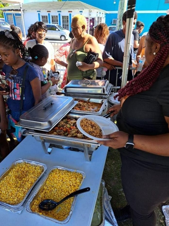 A woman in black holds a plate of rice beside chafing dishes and trays of corn