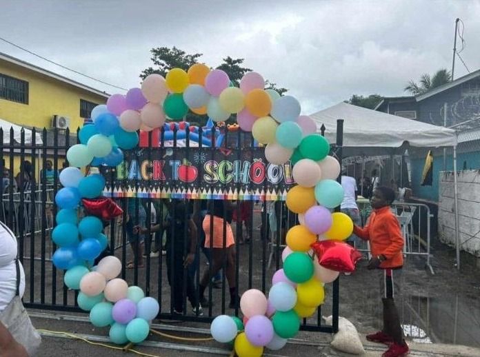 A Back to School balloon arch stands at a gate while a boy in an orange jacket waits outside