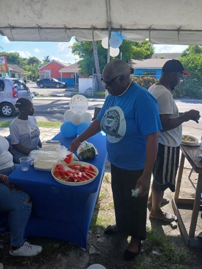 A woman in a blue United Against Crime shirt serves sliced watermelon from a platter at a blue table