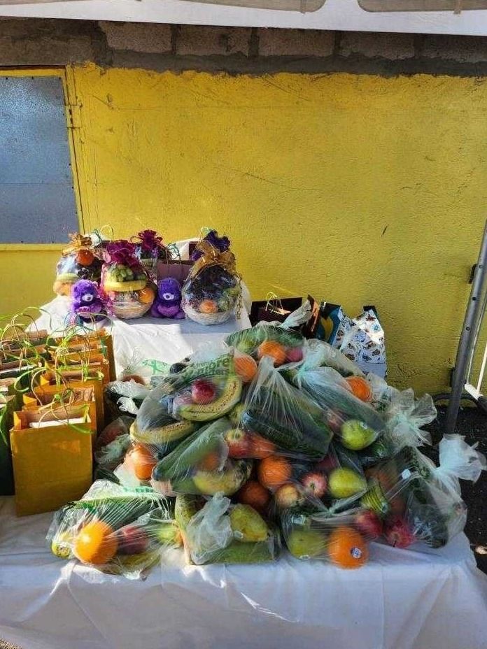 Bags of oranges, bananas, pears and apples are piled on a table in front of gift baskets