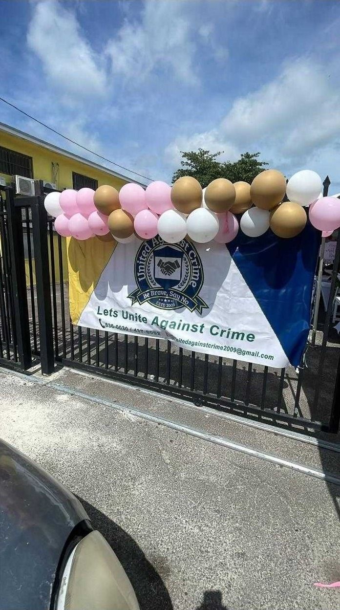 The United Against Crime banner hangs on a black gate under a garland of pink, gold and white balloons