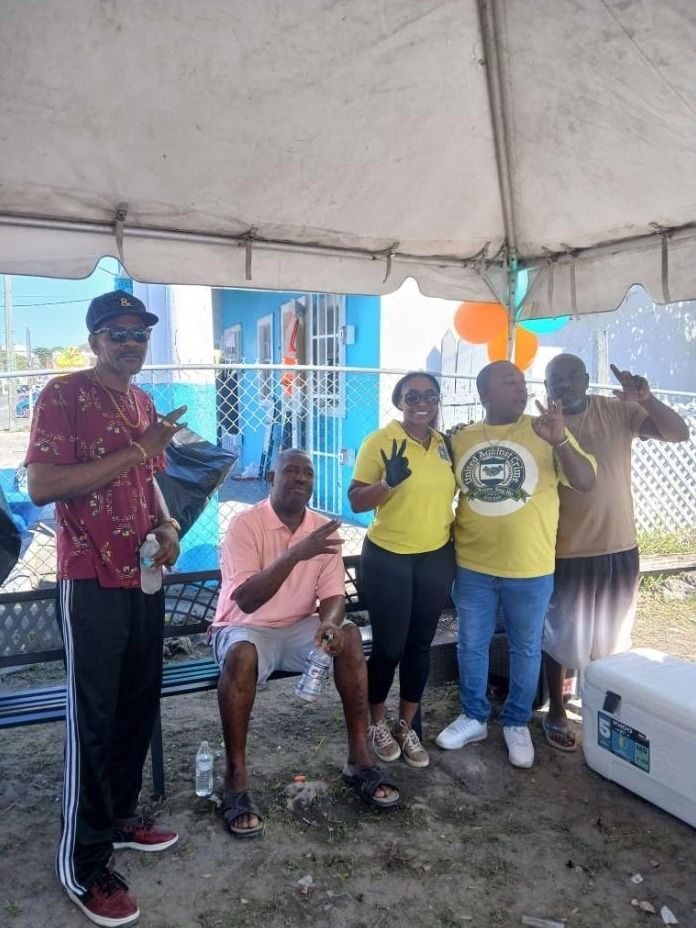A woman in a yellow polo and four men pose with hand signs under the feeding tent