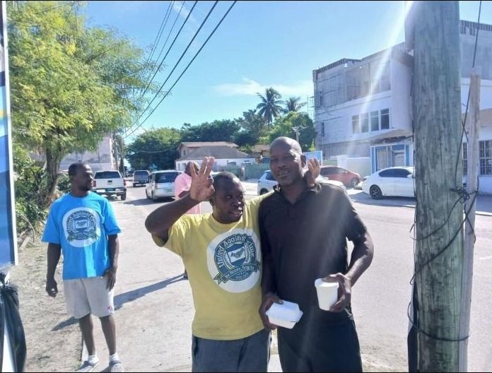 Two men pose in the street holding takeout containers, one wearing a yellow United Against Crime shirt
