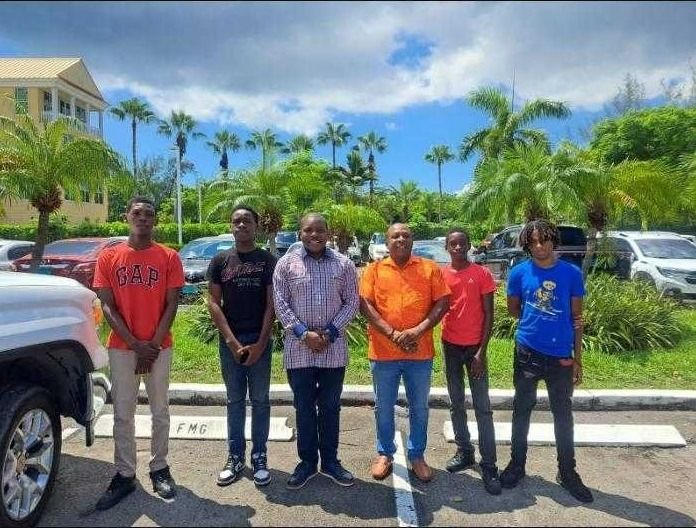Six young men and mentors stand in a row in a parking lot with palm trees before a mentorship tour