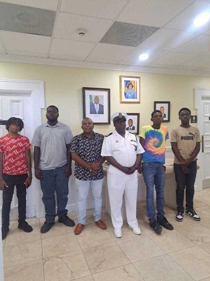 Young mentees and a mentor pose with an officer in a white uniform inside a government office lobby