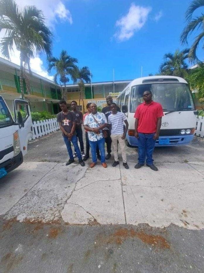 Young participants and mentors stand in front of a white tour bus outside a school building