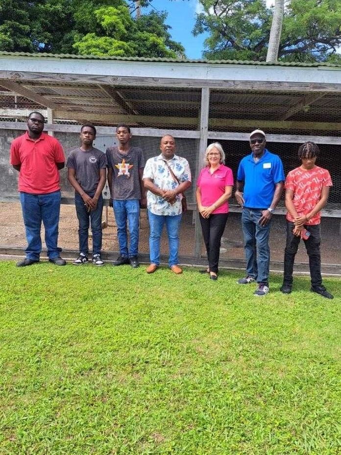 Young participants, mentors and farm staff stand in a line on grass in front of a poultry pen
