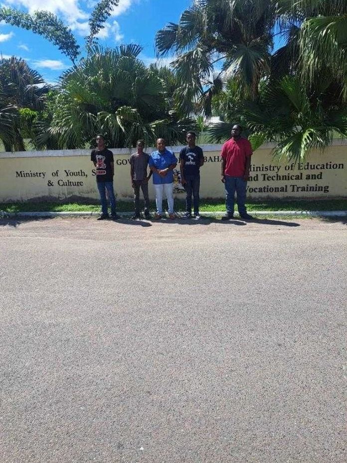 Five people stand in front of a Ministry of Youth, Sports and Culture wall sign